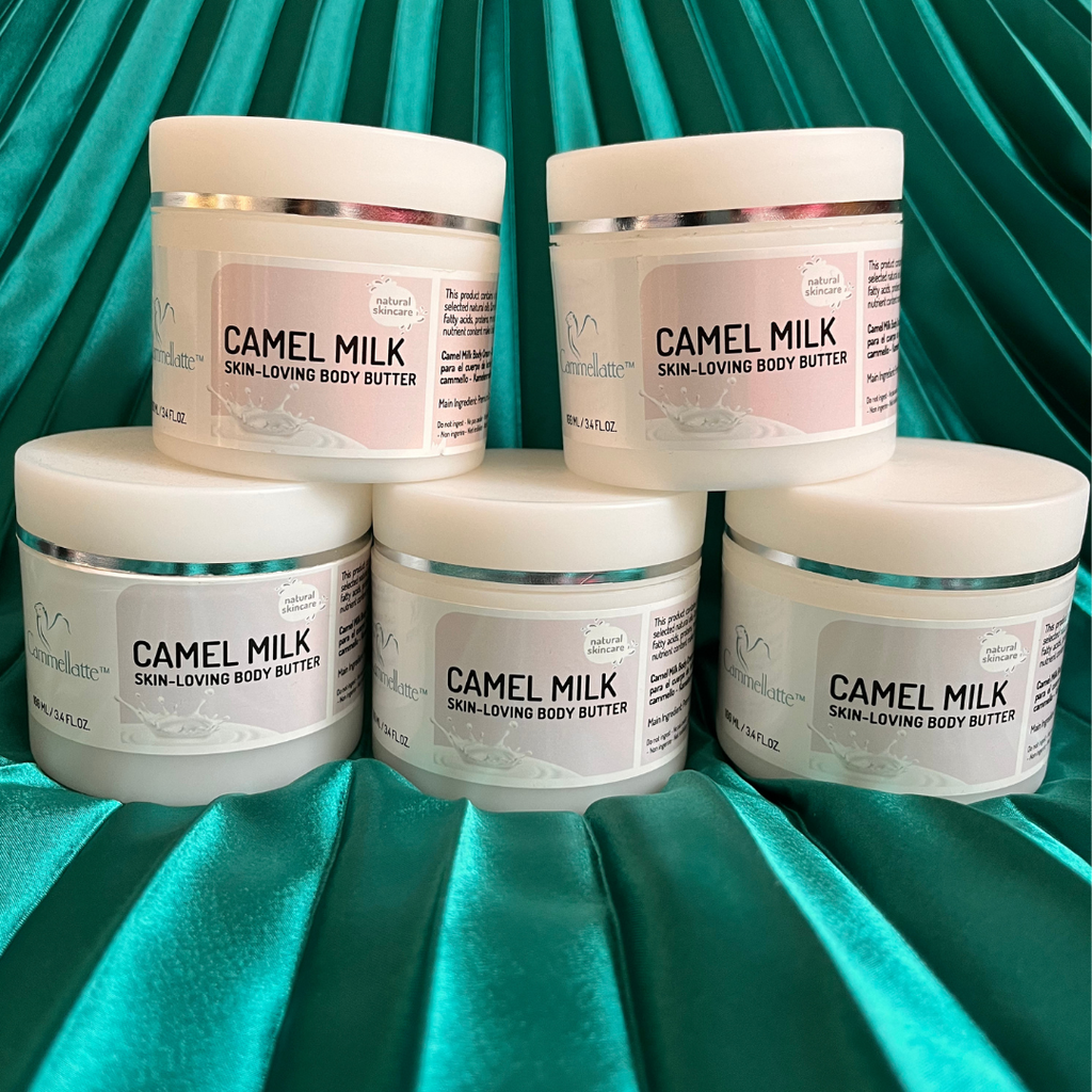 Five jars from the Cammellatte Butter Lover Bundle are stacked on an emerald green satin backdrop. Each jar features a white lid and a light label—ideal for nourishing dry skin.