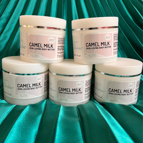 Five jars from the Cammellatte Butter Lover Bundle are stacked on an emerald green satin backdrop. Each jar features a white lid and a light label—ideal for nourishing dry skin.