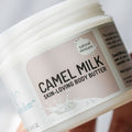A close-up of a white Cammellatte jar labeled Butter Lover Bundle, perfect for dry skin, features a splash of milk design and natural skincare badge. The angled jar is held in someones hand.