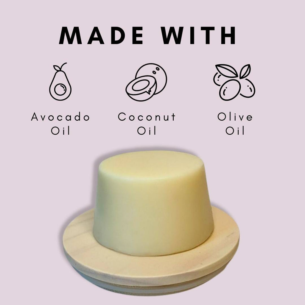 A Camel Milk Face & Body Soap by Cammellatte comes elegantly placed on a wooden dish, infused with camel milk and featuring icons above that highlight its nourishing blend of avocado, coconut, and olive oils. A light pink background enhances the text: MADE WITH camel milk and these enriching oils.