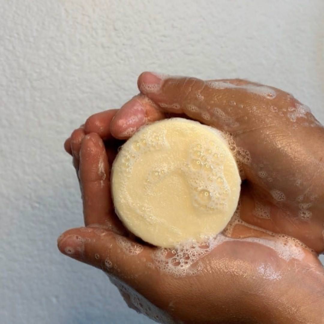 Two soapy hands gently hold a round, creamy Camel Milk Face & Body Soap by Cammellatte against a light background—a luxurious bar and perfect shower gel alternative. Available as a 2-Pack.
